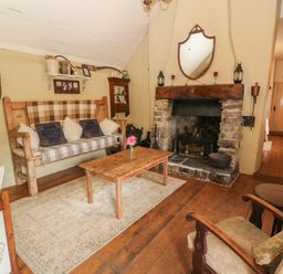 A living room with a stone fireplace wooden furniture and a beige rug at Mary Rose Cottage in Cordal near Castleisland County Kerry