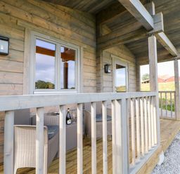 A wooden porch with wicker chairs a table a wine bottle and glass at Badgers Sett in Winston near Staindrop