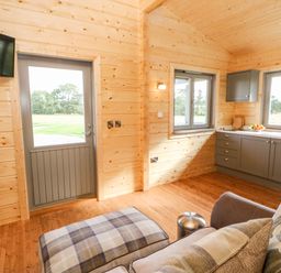 A small wooden living space with a sofa, ottoman, kitchen cabinets, windows, a door, and a wall-mounted TV at Badgers Sett in Winston near Staindrop