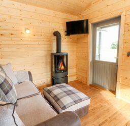 A wooden room with a door a wall-mounted TV a stove sofa and an ottoman with plaid cushions at Badgers Sett in Winston near Staindrop