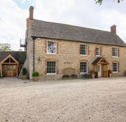 A stone farmhouse with multiple windows and wooden doors with potted plants outside at Shifford Manor Farm in Shifford near Bampton Oxfordshire