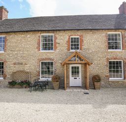 A stone house with six windows a white door with wooden porch and outdoor table and chairs at Shifford Manor Farm in Shifford near Bampton Oxfordshire