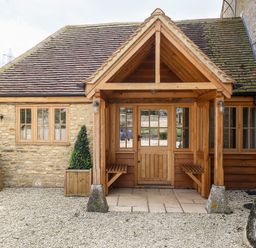 Exterior view of a stone building with a wooden porch and two planters with shrubs at Shifford Manor Farm in Shifford near Bampton Oxfordshire