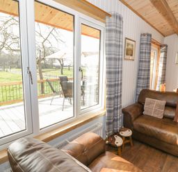 A living room with brown leather sofas cushions small stools dining table and large windows with a view of a garden at Top Style Orchard in Hallow