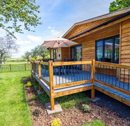 A wooden deck with outdoor chairs a table and an umbrella next to a wooden house at Top Style Orchard in Hallow