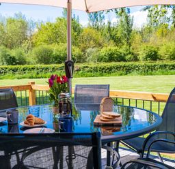 An outdoor glass table with croissants coffee mugs sliced bread and flowers under an umbrella at Top Style Orchard in Hallow