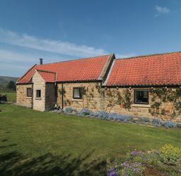 A stone house with red tiled roof surrounded by grassy lawn and flowers at Silver Birches in Glaisdale