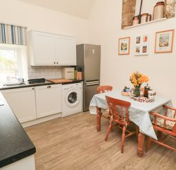 A kitchen with white cabinets a table with flowers and wooden chairs at Silver Birches in Glaisdale