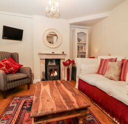 A living room with a striped armchair red cushions a wooden coffee table and a fireplace at October Cottage in Chalford Gloucestershire