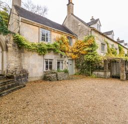 A stone cottage with climbing plants on the walls a gravel driveway and wooden doors at October Cottage in Chalford Gloucestershire