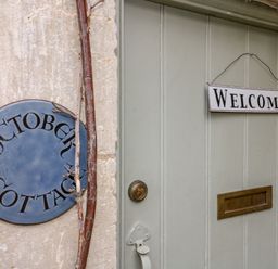 A door with a welcome sign a mail slot and a round sign saying October Cottage on a stone wall at October Cottage Chalford Gloucestershire