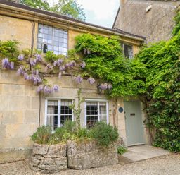 Stone cottage exterior with climbing plants and flowers near a green door at October Cottage in Chalford Gloucestershire