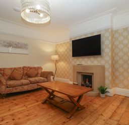 A living room with a sofa coffee table fireplace television and wooden floor at Greenlawns in Burnham-On-Sea