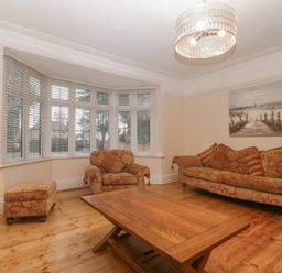 A living room with patterned sofa armchair ottoman wooden coffee table and large bay window at Greenlawns in Burnham-On-Sea