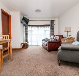 A living room with a red sofa gray armchair wooden side table and dining table at Coach House Cottage in Bude