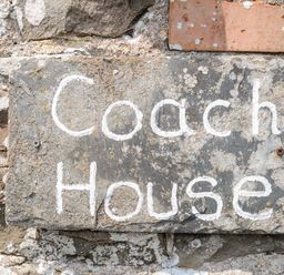 A stone sign with the text Coach House mounted on a brick wall at Coach House Cottage in Bude