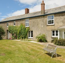 Exterior view of a farmhouse with windows bushes and a bench on the lawn at Lee Barton Farmhouse in Bude