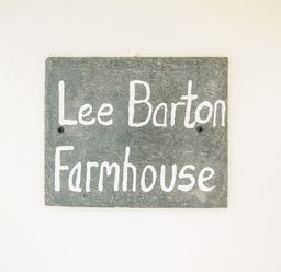 A slate sign with white writing saying Lee Barton Farmhouse on a white wall at Lee Barton Farmhouse Bude