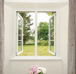 A window with open white frames looking out to a grassy garden with trees and a picnic table at Lee Barton Farmhouse in Bude