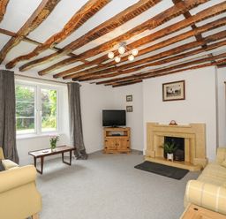 A living room with exposed wooden beams a stone fireplace two sofas a wooden coffee table and a television at Lee Barton Farmhouse in Bude
