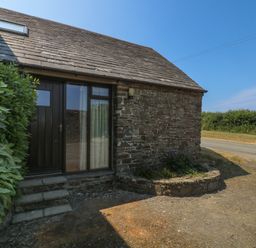 The exterior of a stone house with a wooden door and window next to a small garden bed and a hedge at The Roundhouse in Bude