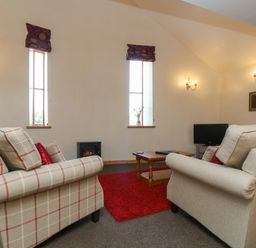 A living room with two sofas a wooden coffee table a red rug and a small television at The Roundhouse in Bude