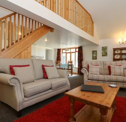 A living room with two sofas red pillows a wooden coffee table red rug and wooden stairs at The Roundhouse in Bude