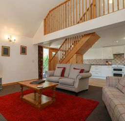 A living room with sofas a wooden coffee table a red rug a television and a staircase leading to an upper floor at The Roundhouse in Bude