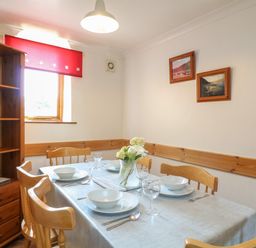 A dining room with a table set for four by a window with a red blind at Swallow Cottage in Bude