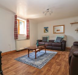 A living room with two leather sofas a wooden coffee table a television and a window with red curtains at Swallow Cottage in Bude