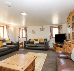A living room with two black sofas a brown armchair a wooden coffee table a television and wooden furniture at The Wagon Linney in Bude