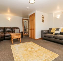 A living room with two leather sofas a wooden coffee table a yellow patterned rug and wooden doors at The Wagon Linney in Bude