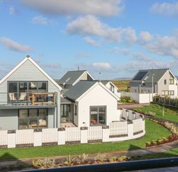 A modern house with a balcony and fenced garden surrounded by grass and a pathway at Devonair in Westward Ho