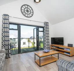 A living room with a sofa coffee table and television by glass doors opening to a balcony at Devonair in Westward Ho