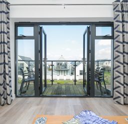 A room with open double glass doors leading to a balcony with chairs and houses visible outside at Devonair in Westward Ho