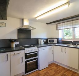 A kitchen with white cabinets, stove, dishwasher, microwave, sink, and window at The Stable in Bude