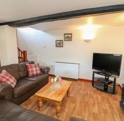 A living room with brown leather sofas a wooden coffee table with a vase of flowers a television on a glass stand and framed pictures on the wall at The Stable in Bude