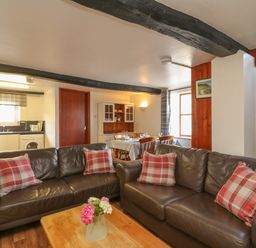 A living room with brown leather sofas and a wooden coffee table with flowers in a vase at The Stable in Bude