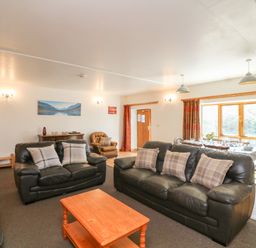 A living room with black leather sofas and a wooden coffee table next to a dining table by a window at The Dairy in Bude