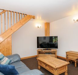 A living room with a blue sofa wooden coffee table tv stand and nested tables at The Shippon in Bude
