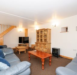 A living room with blue sofas wooden tables a TV a wooden cabinet and stairs at The Shippon in Bude