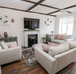 A living room with beige sofas a wall mounted tv a fireplace two sideboards and a window at Martingale in Torquay