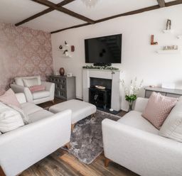 A living room with two armchairs a sofa an ottoman a fireplace a wall-mounted television and wooden flooring at Martingale in Torquay