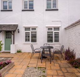 A patio area with a round table and four chairs outside a white building with a green door and three windows at Martingale in Torquay