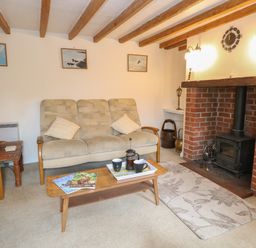 A living room with beige sofas wooden coffee table magazines fireplace and ceiling beams at Primrose Cottage in Stiffkey