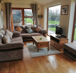 A sitting room with two sofas a coffee table a TV on a stand and large windows showing a garden at Llofft Yr Yd in Llandwrog near Dinas Dinlle