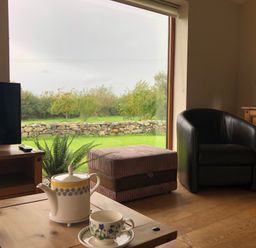 A living room with a teapot and cup on a wooden table overlooking a garden at Llofft Yr Yd in Llandwrog near Dinas Dinlle
