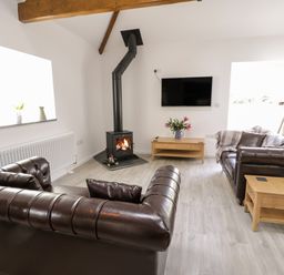A living room with leather sofas a wood burning stove a mounted television and a telescope at 1 Mountain View in Talwrn near Llangefni