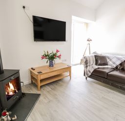 A living room with a wood burning stove a wooden coffee table with flowers and a brown leather sofa at 1 Mountain View in Talwrn near Llangefni