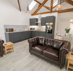 An open plan kitchen and living area with dark grey cabinets brown leather sofas wooden side tables and a dining table with flowers at 1 Mountain View in Talwrn near Llangefni